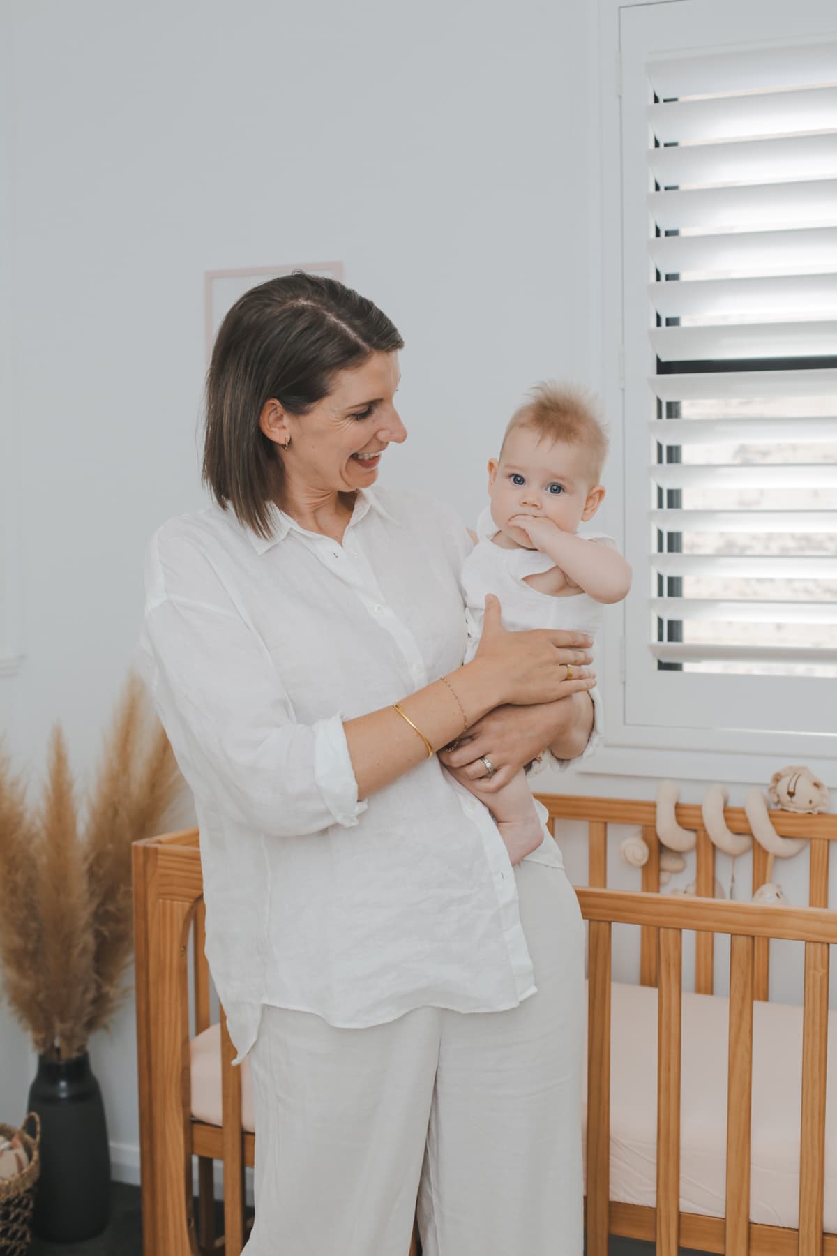 Anna smiling while holding a baby beside a wooden crib